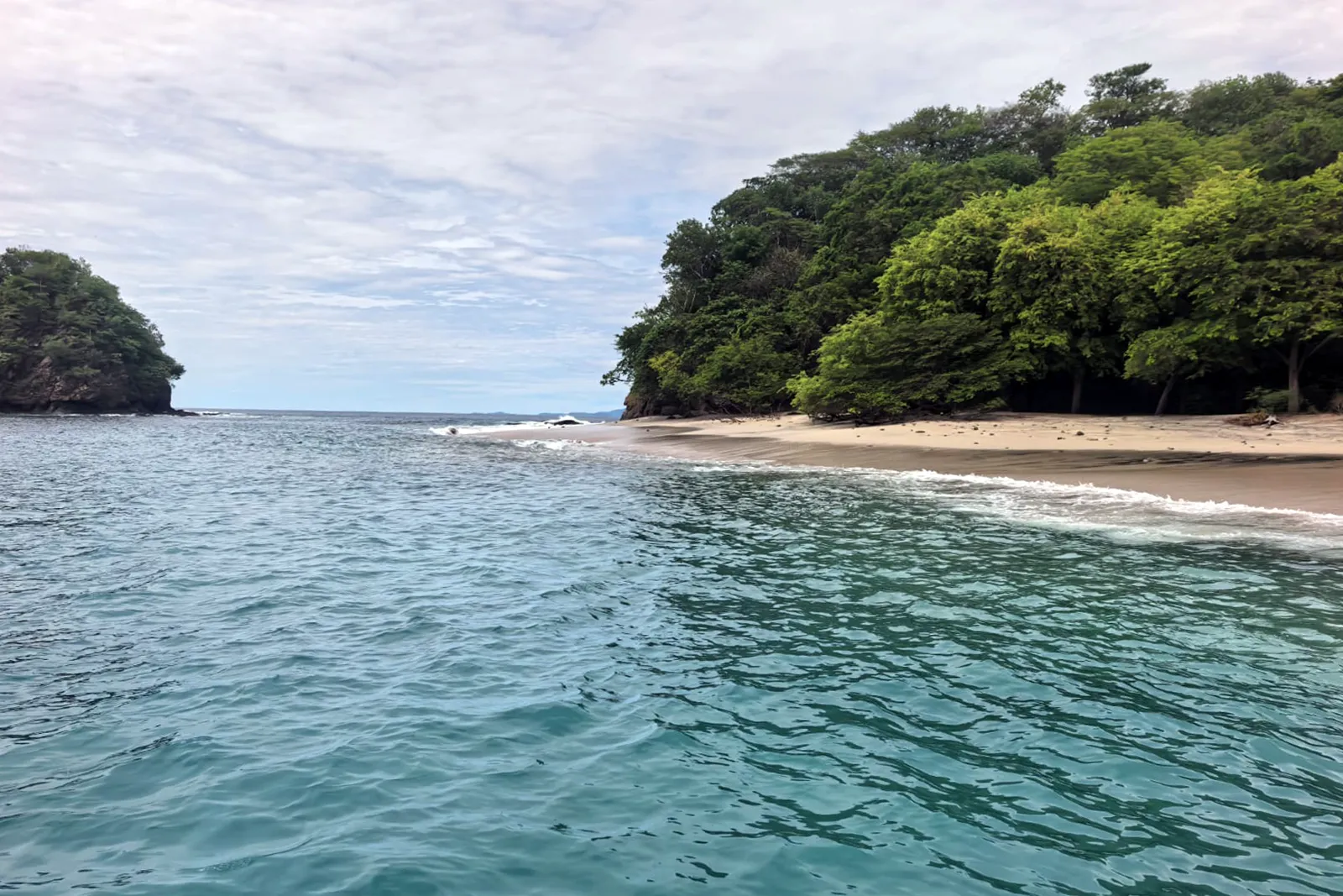 Green headland and sandy beach seen from the water in Papagayo